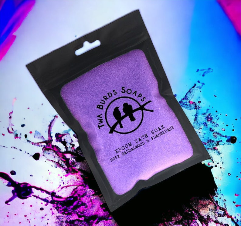 May include: A purple pouch with a black zipper and a white label that says "Twa Burds Soaps" with two birds on a branch and the text "Epsom Bath Soak No.32 Sandalwood & Frangipani".