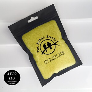 May include: A black resealable pouch filled with yellow bath salts. The pouch has a white label with black text that reads "Twa Burds Soaps Epsom Bath Soak No.41 Rhubarb & Custard".