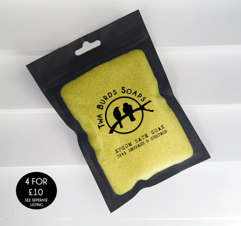 May include: A black resealable pouch filled with yellow bath salts. The pouch has a white label with black text that reads "Twa Burds Soaps Epsom Bath Soak No.41 Rhubarb & Custard".