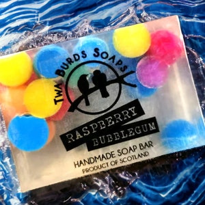 Peut inclure: Une barre de savon transparente au parfum de bubble-gum &agrave; la framboise. Le savon est d&eacute;cor&eacute; de formes rondes color&eacute;es et porte le texte "Twa Birds Soaps" et "Raspberry Bubblegum" ainsi que le texte "Handmade Soap Bar Product of Scotland".