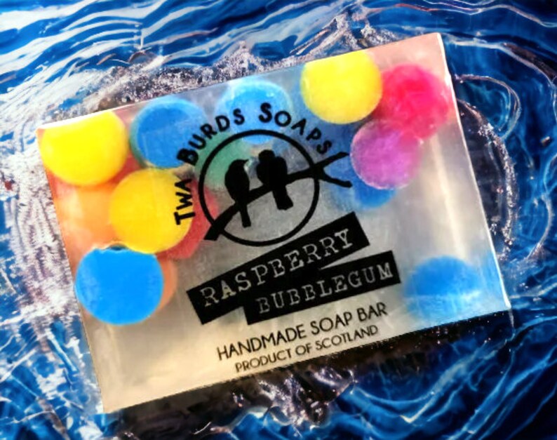 Peut inclure: Une barre de savon transparente au parfum de bubble-gum &agrave; la framboise. Le savon est d&eacute;cor&eacute; de formes rondes color&eacute;es et porte le texte "Twa Birds Soaps" et "Raspberry Bubblegum" ainsi que le texte "Handmade Soap Bar Product of Scotland".