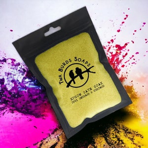 May include: A gold pouch with a black zipper closure and a hanging loop. The pouch has a black and white logo with the text "Twa Burds Soaps" and "Epsom Bath Soak No.41 Rhubarb & Custard".