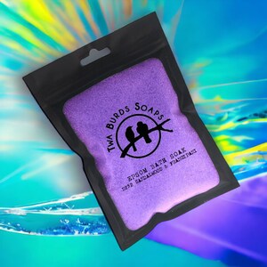 May include: Purple Epsom bath soak in a black resealable bag with a hanging hole. The bag has a white logo with two birds on a branch and the text "Twa Burds Soaps" and "Epsom Bath Soak No.32 Sandalwood & Frangipani".