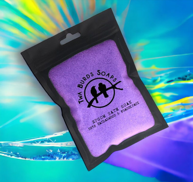 May include: Purple Epsom bath soak in a black resealable bag with a hanging hole. The bag has a white logo with two birds on a branch and the text "Twa Burds Soaps" and "Epsom Bath Soak No.32 Sandalwood & Frangipani".