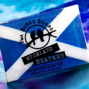 May include: A blue and white bar of soap with a Scottish flag design. The soap is labelled "Twa Birds Soaps Highland Heather Handmade Soap Bar Product of Scotland".