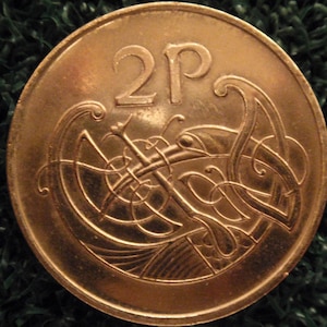 May include: A copper-colored 2 pence coin from the United Kingdom. The coin features a Celtic knot design.