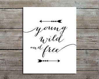 May include: A rectangular white sign featuring the black text "young wild and free" in a cursive script font. The text is centered between two horizontal black arrows, each pointing in opposite directions, with decorative circular accents.