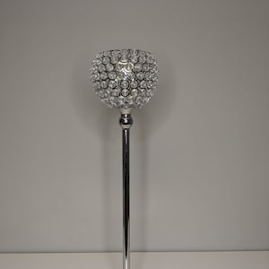 May include: A tall, silver candle holder with a round, crystal-encrusted base. The holder is designed to hold a single candle.