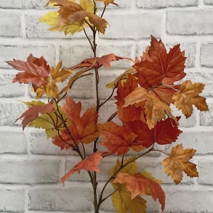 May include: An artificial maple branch featuring a collection of vibrant autumn-colored leaves in shades of deep red, burnt orange, and golden yellow. The branch has a thin, brown stem that supports multiple stems with serrated foliage.