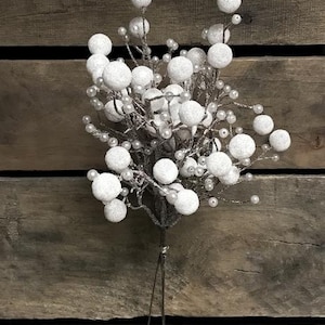 May include: A decorative floral stem with clusters of white, snow-covered balls and small pearl-like beads. The stem is dark brown and has thin wire stems, set against a rustic wooden background. Suitable for festive decorations.