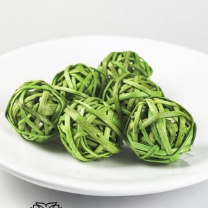 May include: Six green woven balls made of natural materials, displayed on a white plate. The balls are round and have a textured surface.