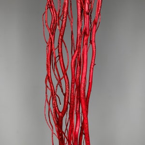 May include: A collection of vertical, slender branches coated in a vibrant red finish with a fine layer of sparkling glitter. The branches feature a natural, twisted, and organic structure with multiple thin offshoots extending from the main stems.