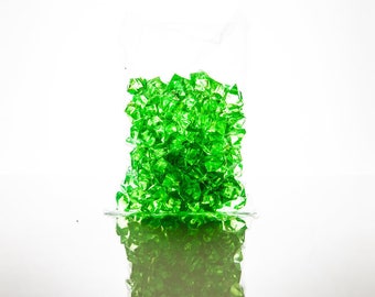 May include: A clear plastic bag filled with bright green crystal-like gems. The gems are reflecting light and creating a sparkling effect.
