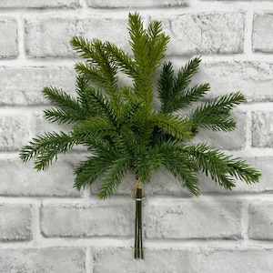 May include: A green artificial pine branch spray featuring multiple needle-covered stems radiating from a central point. The stems are bound together at the base with a thin wire and a small piece of twine, creating a fan-like arrangement.