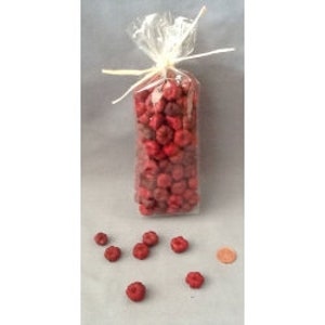 May include: A clear cellophane bag tied with raffia, filled with small, round, red objects. Several of the red objects are scattered in front of the bag. A penny is next to the scattered objects.