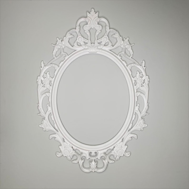 May include: White ornate oval picture frame with a decorative, intricate design. The frame is made of a smooth, white material and has a classic, elegant style.