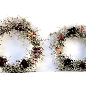 May include: Two dried flower wreaths with a variety of dried flowers in shades of pink, purple, and black. The wreaths are made with dried grasses and are perfect for a rustic or farmhouse decor style.