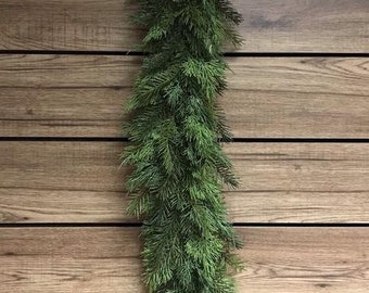 May include: A long, green garland of artificial pine branches, hanging against a wood panel background.