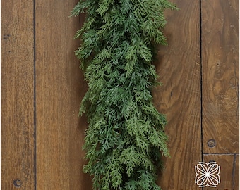 May include: A long, green garland of artificial cedar branches, hanging against a woodgrain background. The garland is perfect for adding a touch of greenery to your home decor.