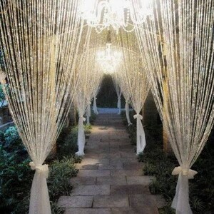 May include: A walkway lined with white fabric and crystal beaded curtains, illuminated by hanging chandeliers.