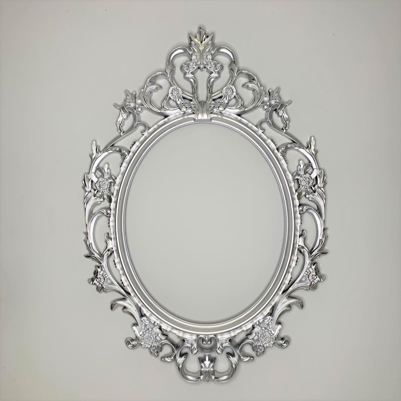 May include: A silver oval-shaped picture frame with an ornate design. The frame has a decorative top with a crown-like design and floral details.