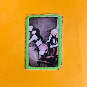 Puede incluir: Un parche enmarcado en verde con una imagen en blanco y negro de dos personas en un ambiente vintage. La imagen es de estilo retro.