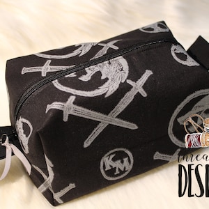 May include: Black zippered pouch with a repeating pattern of silver swords and a winged creature. The pouch has a black zipper pull and a black strap. The text "threadpool DESIGNS" is visible in the lower right corner.