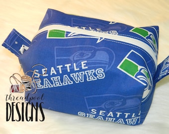 Puede incluir: Bolsa azul y verde con cremallera con el logotipo de los Seattle Seahawks y las palabras "Seattle Seahawks" repetidas en la tela.