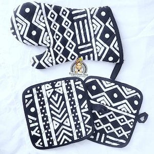 May include: A set of black and white oven mitts and pot holders with a geometric pattern. The mitts and holders are quilted and have a loop for hanging. The text "Rural African Shop" is visible in the image.
