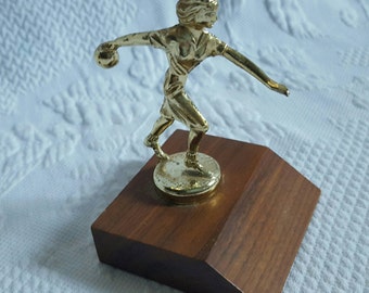 May include: A gold-colored trophy of a woman bowling, standing on a wooden base.