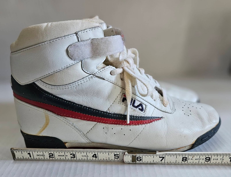 May include: White leather high-top trainers with a blue and red stripe, a velcro strap, and the word "FILA" on the side.