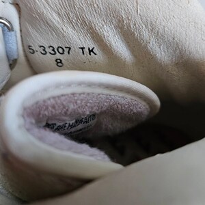 May include: Close-up of the inside of a white shoe with a white fuzzy lining. The size 8 shoe has the text "5-3307 TK" printed on the inside.