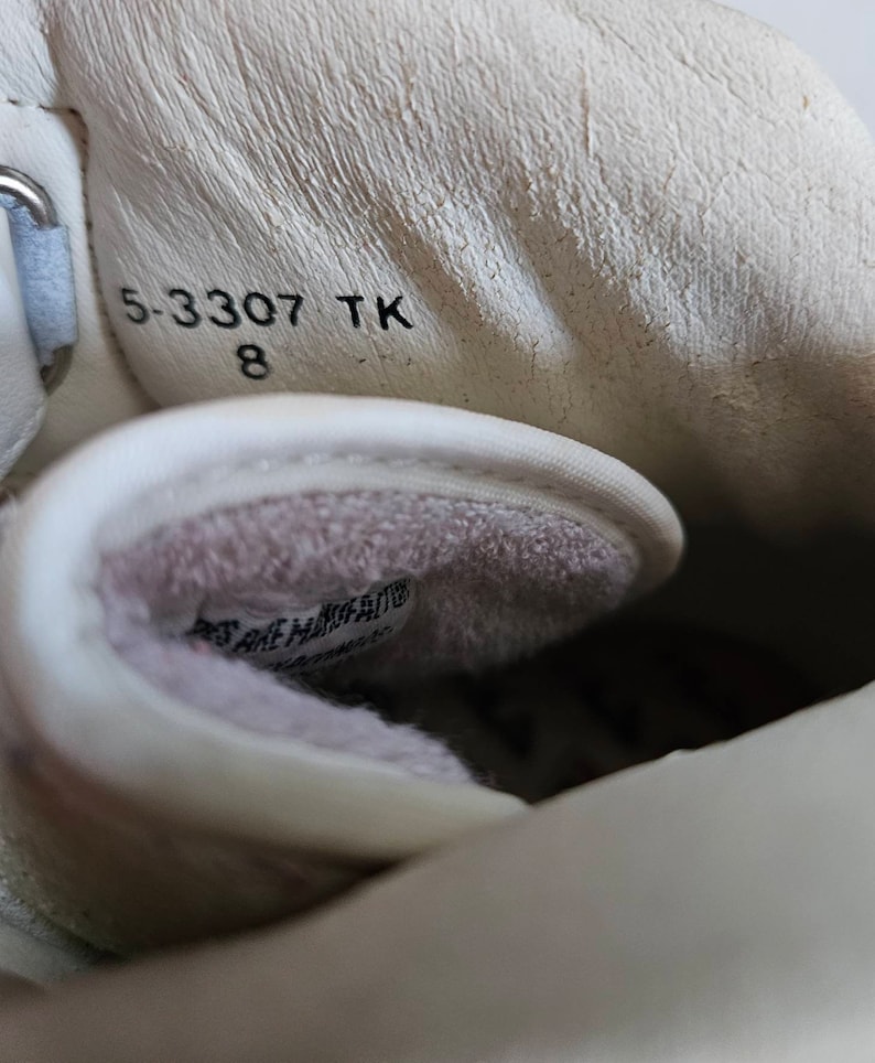 May include: Close-up of the inside of a white shoe with a white fuzzy lining. The size 8 shoe has the text "5-3307 TK" printed on the inside.