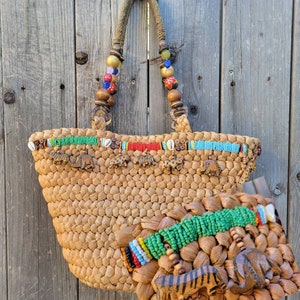 May include: A woven straw tote bag with colorful beaded trim and wooden animal figures. The bag has a brown leather handle with colorful beads.