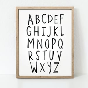 May include: A framed print featuring a black and white alphabet in a handwritten style. The letters are large and bold, with a white background.