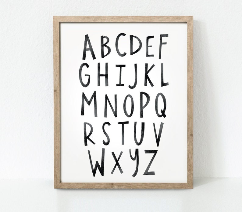 May include: A framed print featuring a black and white alphabet in a handwritten style. The letters are large and bold, with a white background.