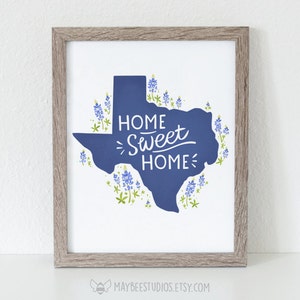 K&ouml;nnte beinhalten: Ein gerahmter Druck mit einer blauen Silhouette des Bundesstaates Texas, umgeben von blauen Lupinen. Der Text "Home Sweet Home" ist in einer stilisierten Schrift innerhalb der Staatsumrisse geschrieben.