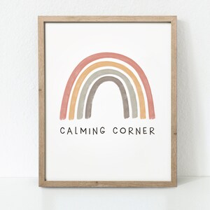 May include: A framed print with a rainbow in shades of pink, orange, yellow, gray, and brown. The rainbow is painted in a watercolor style. The text "CALMING CORNER" is printed below the rainbow.