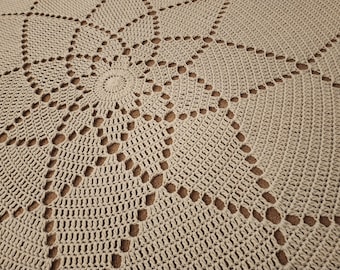 Puede incluir: Primer plano de una alfombra redonda de crochet beige con un patrón circular. La alfombra tiene un diseño delicado y de encaje con detalles calados.