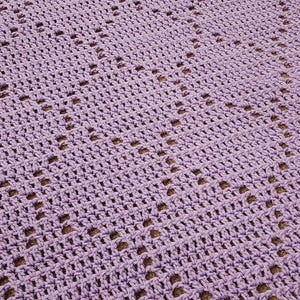 May include: A close-up of a crocheted blanket in a light purple color. The blanket has a diamond pattern with open spaces.