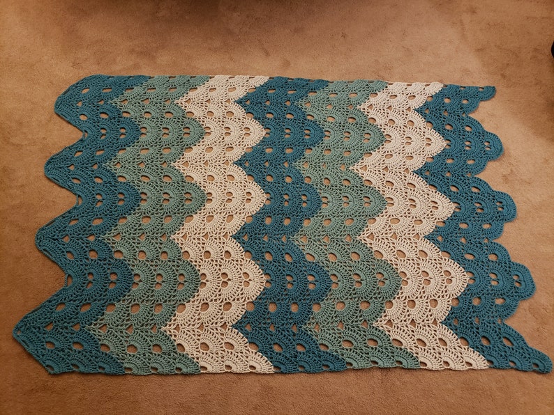 May include: A crocheted blanket with a chevron pattern in shades of teal, green, and white.