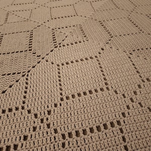 May include: A close-up of a crocheted throw blanket with a diamond pattern in a light brown color.