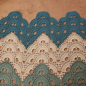 May include: A crocheted blanket with a chevron pattern in teal and beige. The blanket has a scalloped edge.