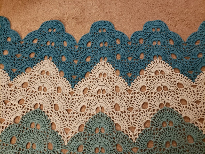 May include: A crocheted blanket with a chevron pattern in teal and beige. The blanket has a scalloped edge.