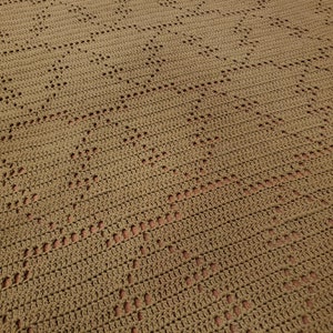 May include: A close-up of a crocheted blanket with a diamond pattern in a brown color.