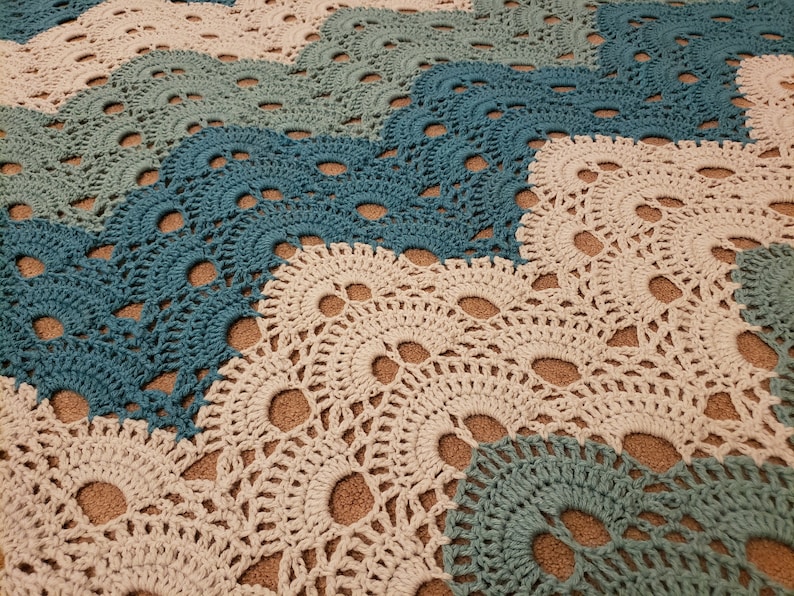 May include: A crocheted blanket with a wavy pattern in shades of teal, blue, and cream.