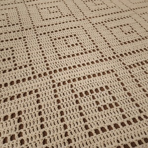 May include: A close-up of a crocheted blanket with a square pattern in a cream colour.