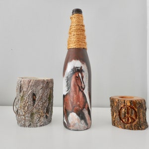 May include: A brown glass bottle with a horse painted on it, wrapped in twine. Two wooden candle holders, one with a peace sign carved into it.