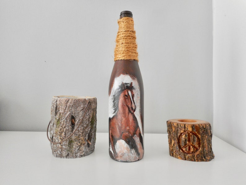May include: A brown glass bottle with a horse painted on it, wrapped in twine. Two wooden candle holders, one with a peace sign carved into it.