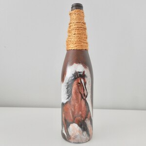 May include: A brown glass bottle with a brown horse painted on it. The bottle is wrapped with twine around the neck.
